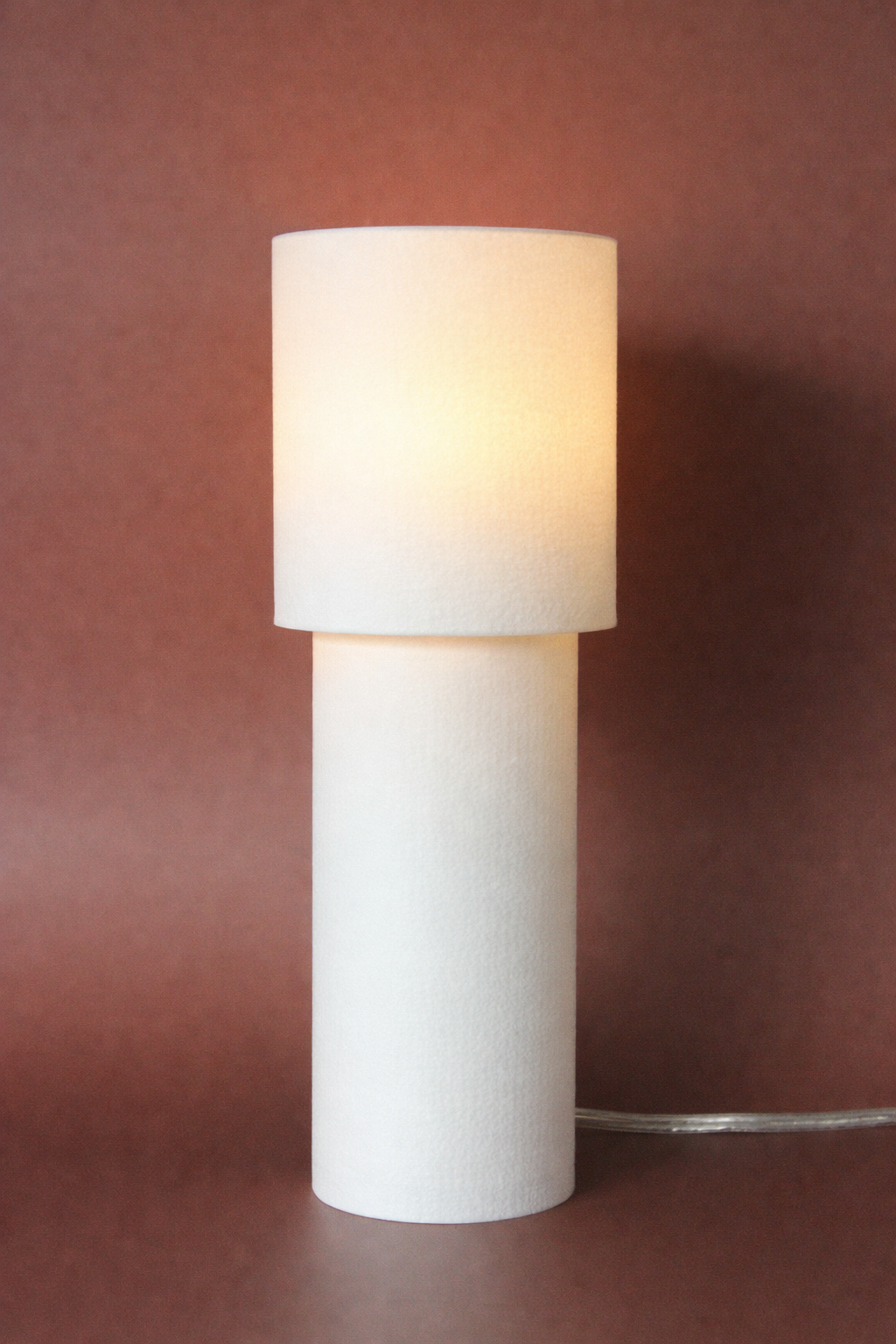 White table lamp with a cylindrical base and round shade on a brown background