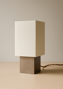 Minimalist table lamp with a beige square shade on a matching base against a beige background